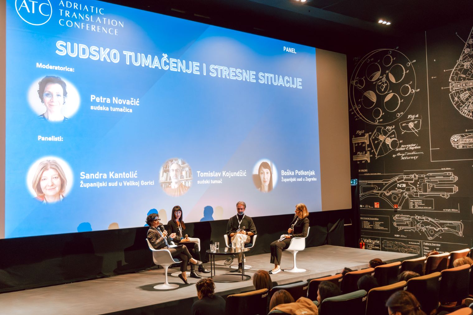 Četiri osobe sede na stolicama na bini i ekran na kojem piše Sudsko tumačenje i stresne situacije